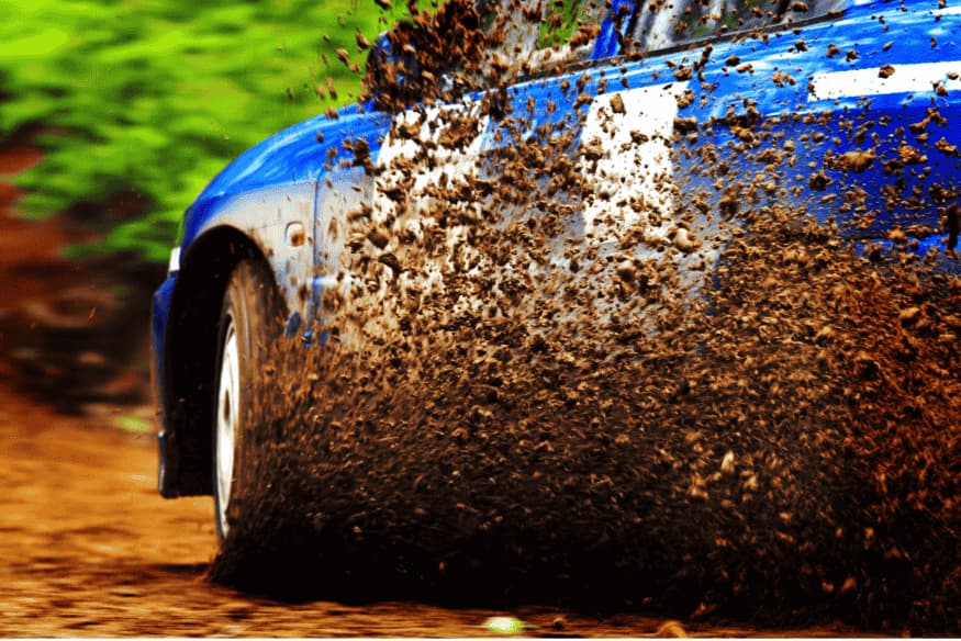 Carro de rally acelerando em alta velocidade na terra, levantando uma enorme quantidade de lama e barro.