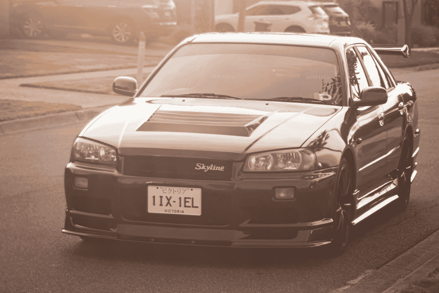 Nissan Skyline R34 preto estacionado em uma rua residencial ao pôr do sol