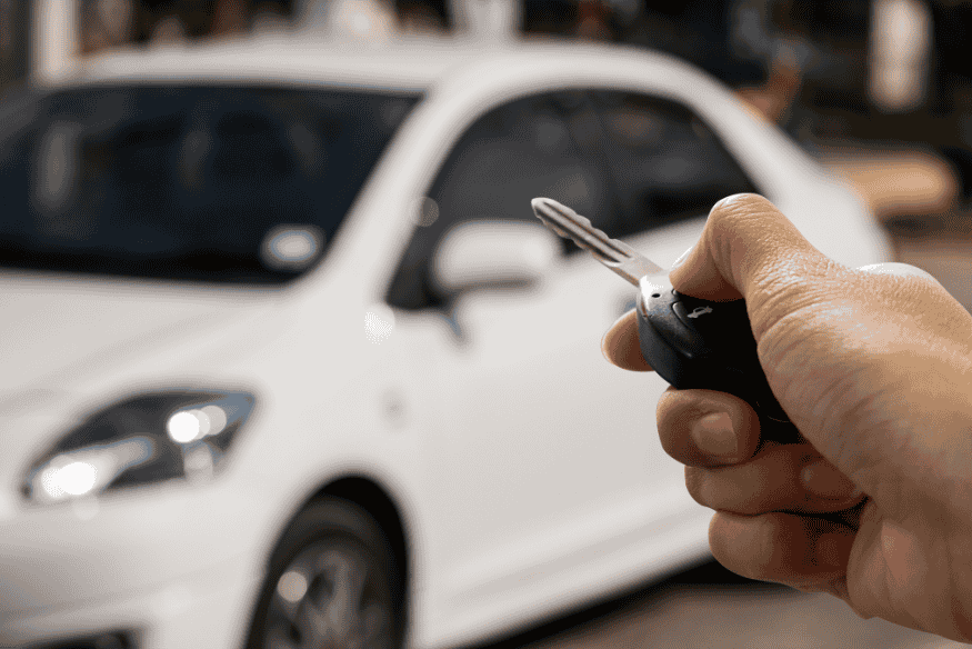 Pessoa segurando chave de carro apontando para um veículo branco desfocado.