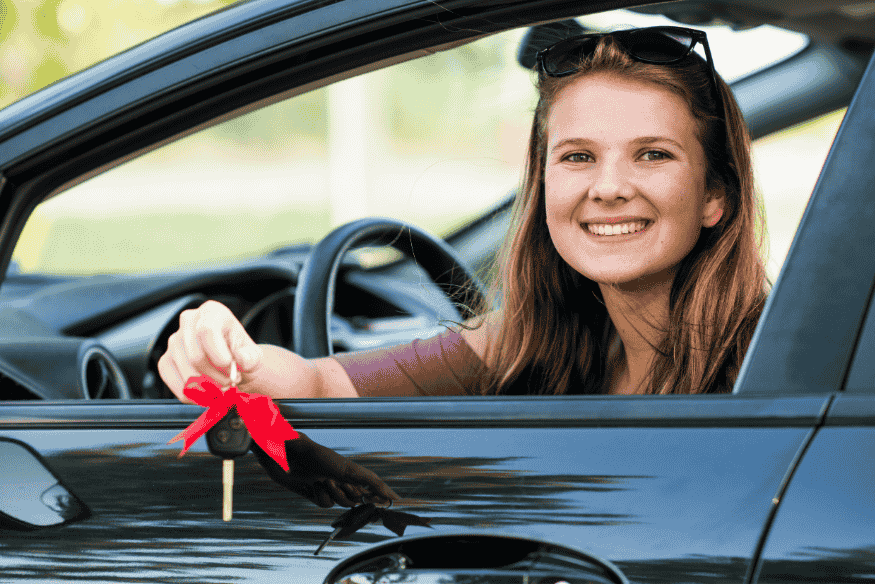 Jovem sorridente dentro do carro segurando uma chave com laço vermelho.