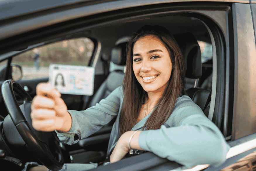Jovem motorista segurando a CNH com sorriso, dentro do carro.