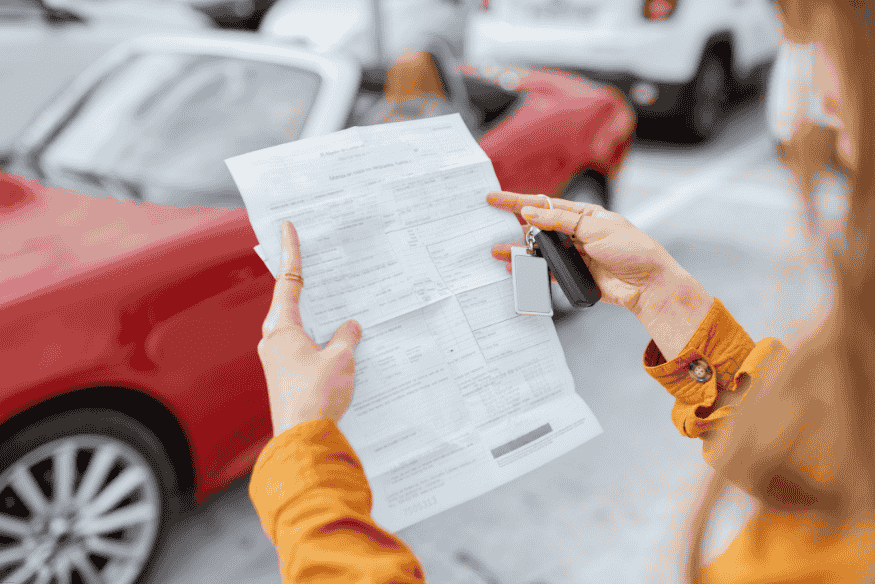 Pessoa segurando documento veicular e chave de carro em estacionamento, analisando informações antes da compra.