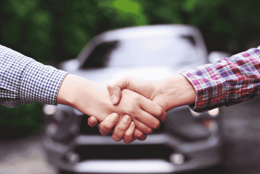 Aperto de mãos entre duas pessoas em frente a um carro, simbolizando a conclusão de uma negociação de compra