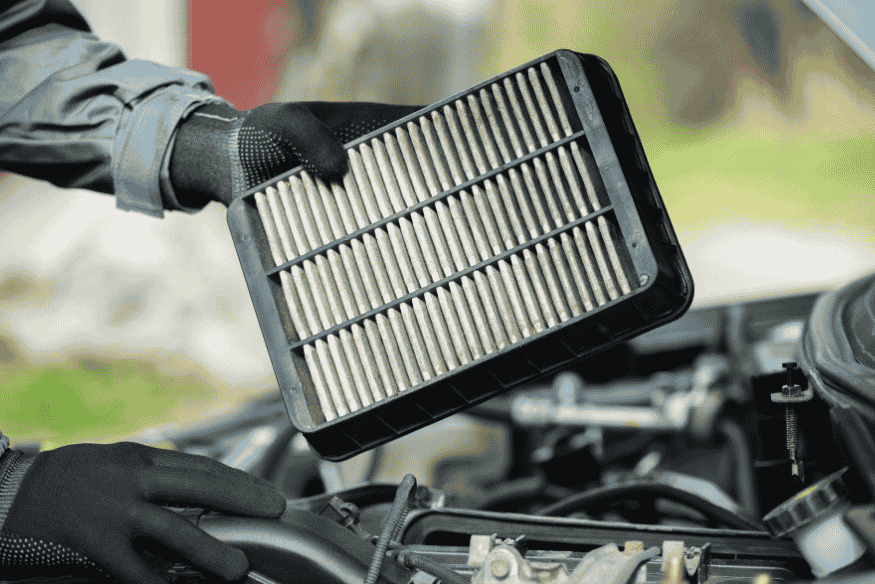 Mão segurando filtro de ar do motor sujo, prestes a ser trocado durante manutenção.