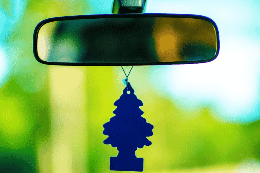 Aromatizador de ambiente em formato de pinheiro azul pendurado no espelho retrovisor de um carro.
