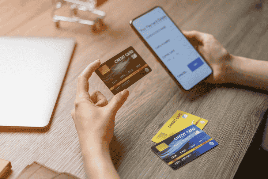 Pessoa segurando cartões de crédito e realizando pagamento online em smartphone.
