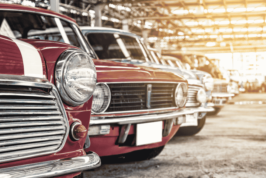 Detalhe de carros clássicos alinhados em exposição coberta com iluminação natural