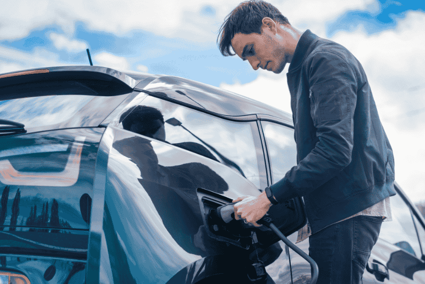 Homem conectando um carro elétrico a um ponto de recarga em ambiente externo.
