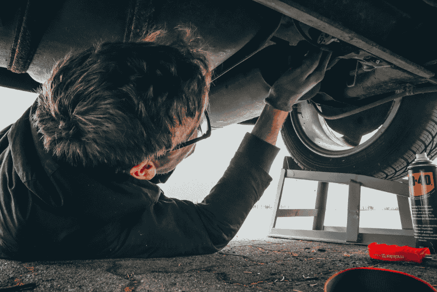 Pessoa deitada no chão realizando manutenção embaixo de um carro com ferramentas ao lado.
