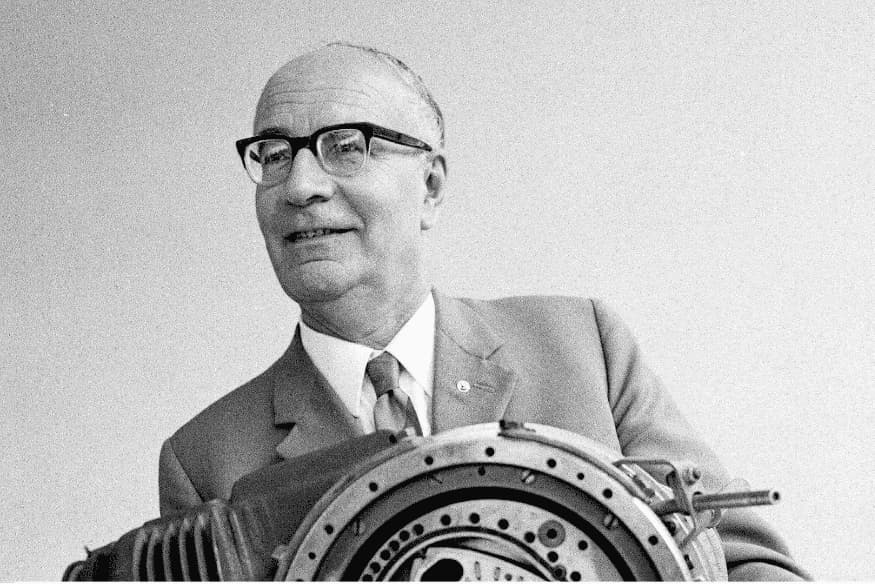 Felix Wankel segurando um motor rotativo, sorrindo em um retrato em preto e branco.