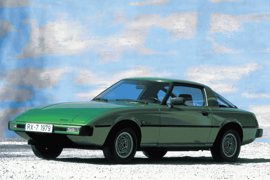 Mazda RX-7 de 1979 na cor verde estacionado sob fundo artístico.
