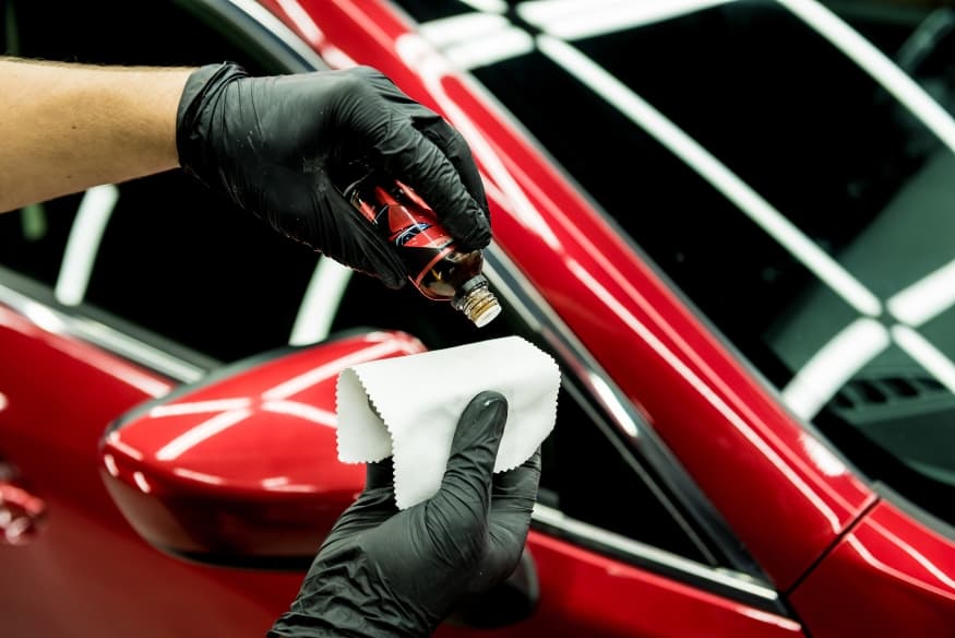 Profissional aplicando revestimento cerâmico em carro vermelho com pano e luvas