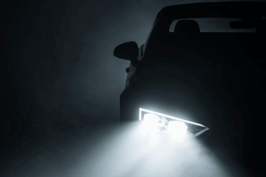 Veículo moderno com faróis de LED iluminando uma estrada com névoa densa durante a noite.