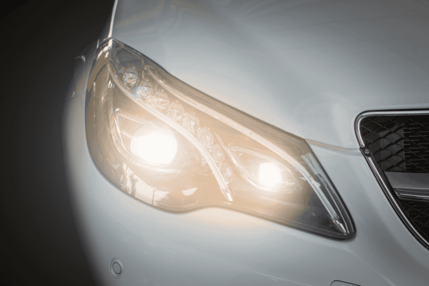 Farol LED moderno aceso em um veículo branco, destacando o design sofisticado e a intensidade da luz.