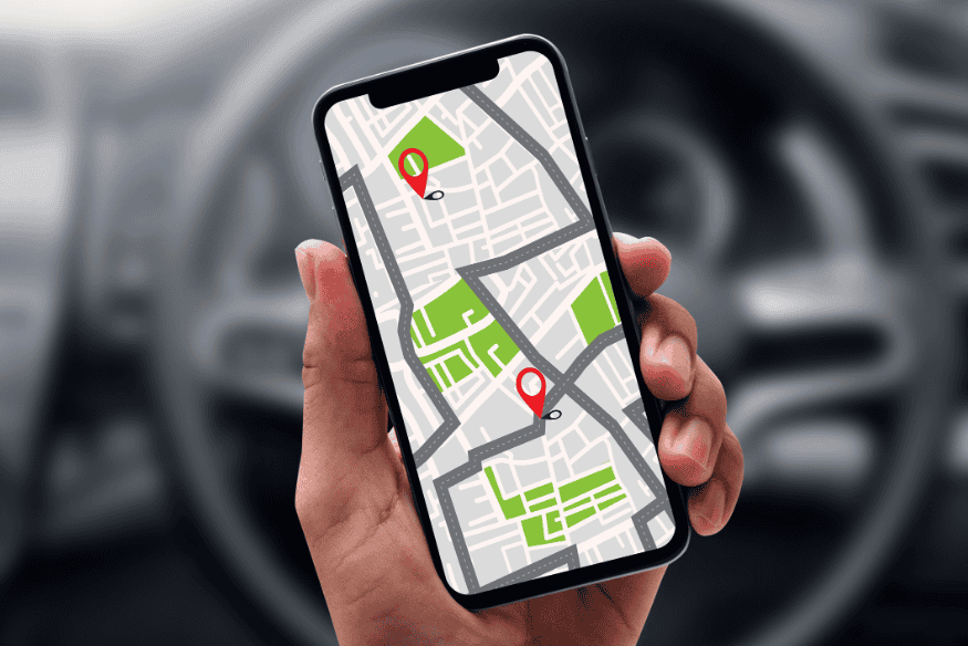 Pessoa segurando um smartphone com mapa GPS na tela, em frente ao volante de um carro.