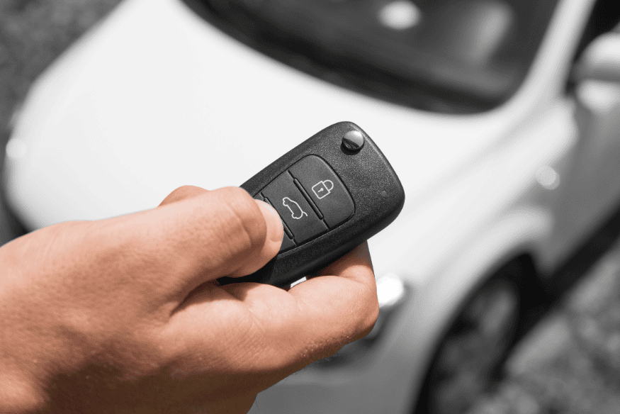Pessoa segurando controle remoto de alarme veicular apontado para um carro branco