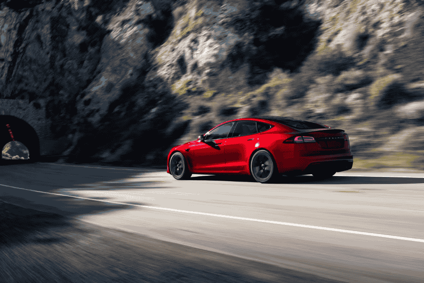 Tesla Model S vermelho em alta velocidade, dirigindo por uma estrada montanhosa.