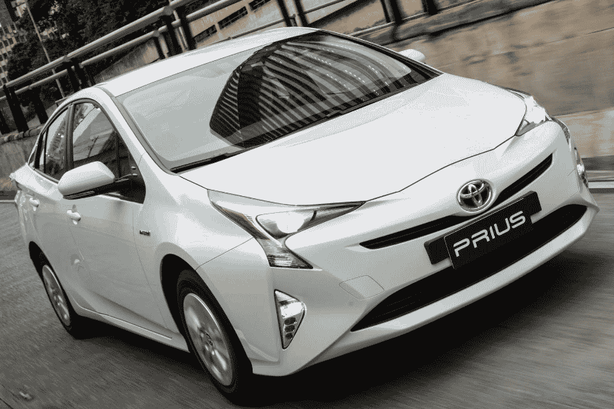 Toyota Prius branco circulando em via urbana com prédios ao fundo.