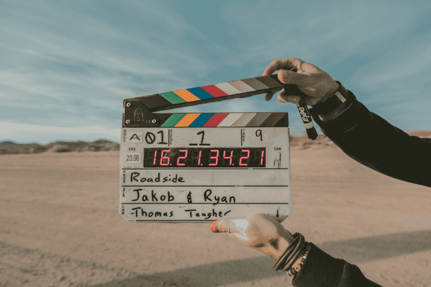 Claquete de cinema digital sendo segurada por uma pessoa no meio de um deserto, com céu azul ao fundo.